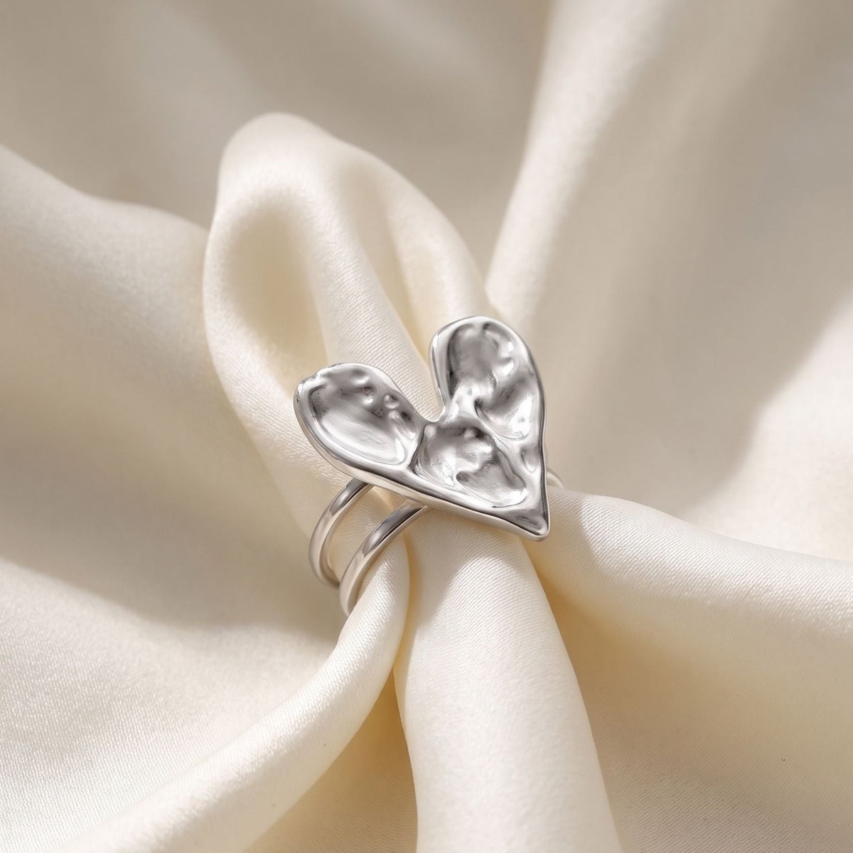 Bague cœur argentée posée sur un satin